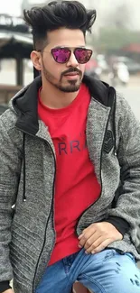 Man in urban fashion with red shirt and gray jacket sitting on a moped.