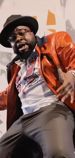 Man in orange jacket with hat striking a pose against abstract background.