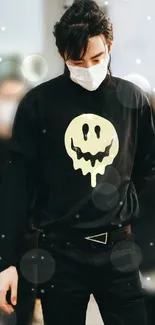 Man with black T-shirt featuring a yellow smiley face design, wearing a mask.