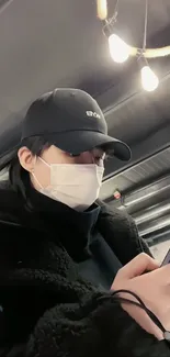 Stylish individual using phone in urban setting, wearing cap and mask.