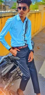 Young man in sunglasses posing by a vibrant yellow wall with a motorcycle.