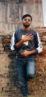 Man in casual wear leaning on a rustic brick wall.