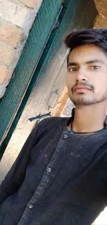 Young man in black outfit against a brick wall and green door.