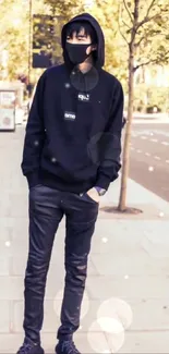 Masked individual in hoodie on urban sidewalk with trees.