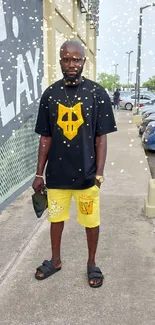 A man in yellow urban streetwear poses on a city sidewalk.