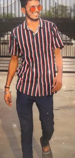 Person wearing stylish striped shirt with sunglasses, walking outdoors.