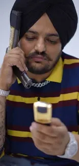 Man in striped shirt with phone and gun accessory.