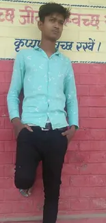 Young man in blue shirt leaning on red brick wall.