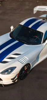 A sleek white sports car with blue racing stripes against a dark pavement.