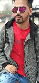 Man in gray jacket and red shirt posing stylishly outdoors.