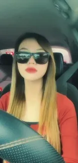 A stylish woman driving, wearing sunglasses and a red shirt.