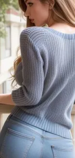 Woman wearing a gray knit sweater on a balcony.