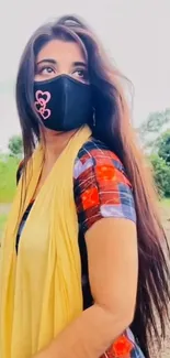 Woman with long hair, wearing a mask and plaid shirt in nature.