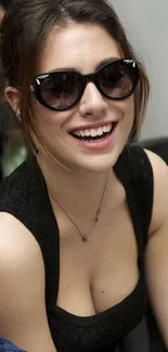 Woman in sunglasses smiling vibrantly in a stylish black outfit.