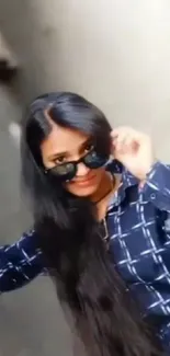 Stylish woman with sunglasses and long hair in a patterned blue shirt.