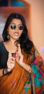 Woman in colorful saree with sunglasses, posing indoors.