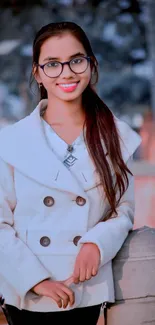 Woman wearing a chic white coat and glasses in an outdoor setting.