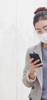 Woman in plaid coat using smartphone against light gray wall.