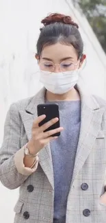 Woman in blazer using smartphone against a light background.