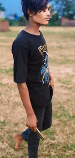 Young man in black outfit standing in a grassy outdoor setting.