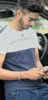 Young man leaning on car, using smartphone.