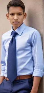 Young professional in blue shirt and tie, leaning against a beige wall.