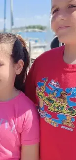 Kids smiling in colorful outfits at a sunny harbor scene.