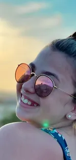 Girl smiling in sunglasses with a sunset background.