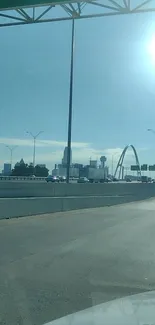 City road with skyline and iconic arch under sunny sky.