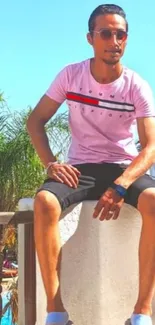 Man sitting outdoors under bright sun wearing casual clothes, surrounded by nature.