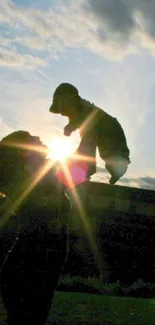 Silhouette of person lifting a puppy against a bright sunset sky.