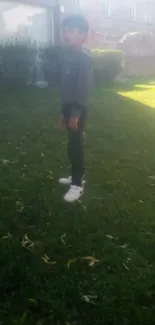 Boy standing on grass under sunlight in an urban garden scene.