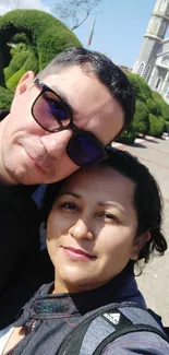 Two friends smiling on a sunny day with a church in the background.