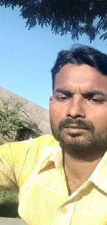 Man in yellow shirt under a bright blue sky with tree shade.