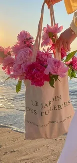 Tote bag with pink flowers on a beach at sunset.