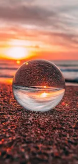 Glass sphere on beach at vibrant sunset.