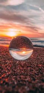 Glass sphere reflecting sunset on a sandy beach with vibrant colors.