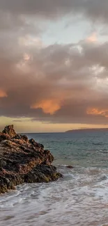 Serene sunset over a rocky beach with vivid clouds and gentle waves.