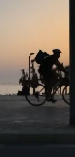 Silhouette of a cyclist riding by the sea at sunset with golden sky.