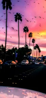 Vibrant sunset over a boulevard with palm trees and distant mountains.