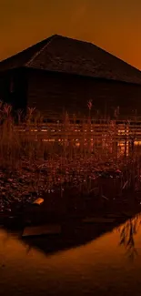 Lakeside cabin at sunset with orange sky.