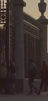 Silhouetted city gate during sunset with people walking by.