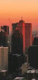 City skyline at sunset with orange sky and silhouettes of buildings.