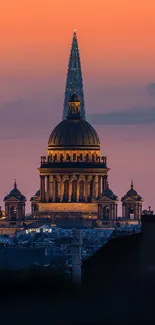 Stunning sunset cityscape with illuminated architecture and vibrant orange sky.