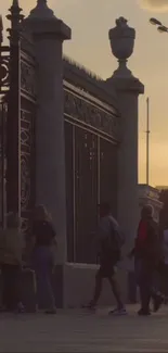 Silhouetted city crowd against a sunset near an ornate gate.