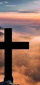 Cross silhouette against a sunset on a misty mountain.