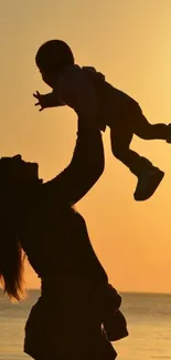 Silhouette of parent lifting child at sunset by the ocean.