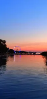 Beautiful sunset over river with Ferris wheel reflection and vibrant sky.