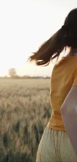 Woman in yellow top walking through a golden wheat field at sunset.