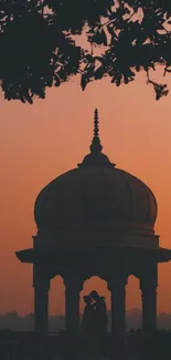 Gazebo silhouette against orange sunset sky.